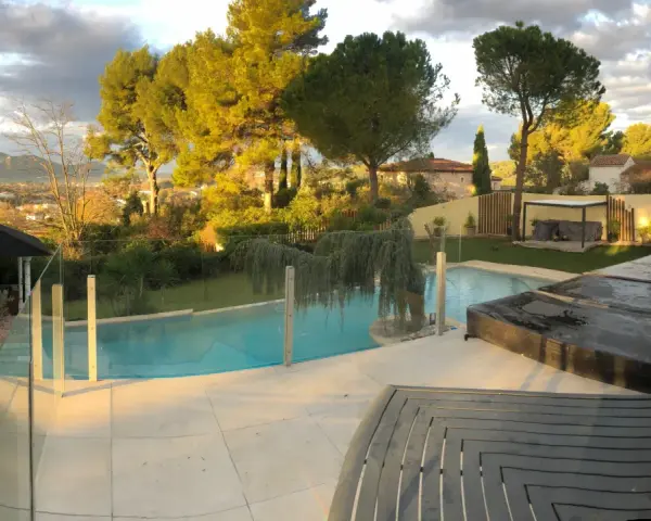 Solnedgång över en pool med trall runt om. Vackert landskap med träd och berg i bakgrunden.