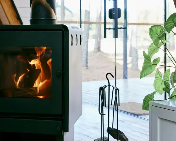 En modern kamin med sprakande eld. Bredvid står en växt och en uppsättning verktyg, allt enligt eldstadsplan regler för säkerhet.