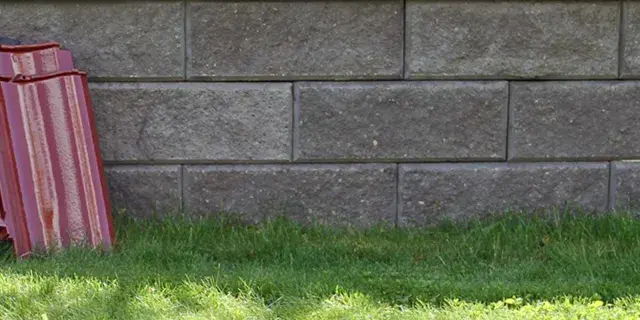 Två staplar takpannor, en svart och en röd, lutar mot en mur av grå betongblock. Undrar vad kostar takpannor?