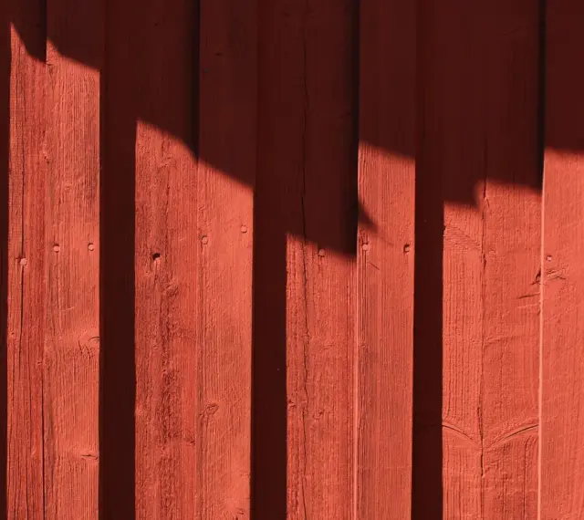 Röda träpaneler med skuggor som faller. Kanske är det dags att måla huset igen?