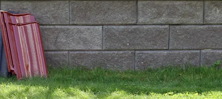 Två staplar takpannor, en svart och en röd, lutar mot en mur av grå betongblock. Undrar vad kostar takpannor?