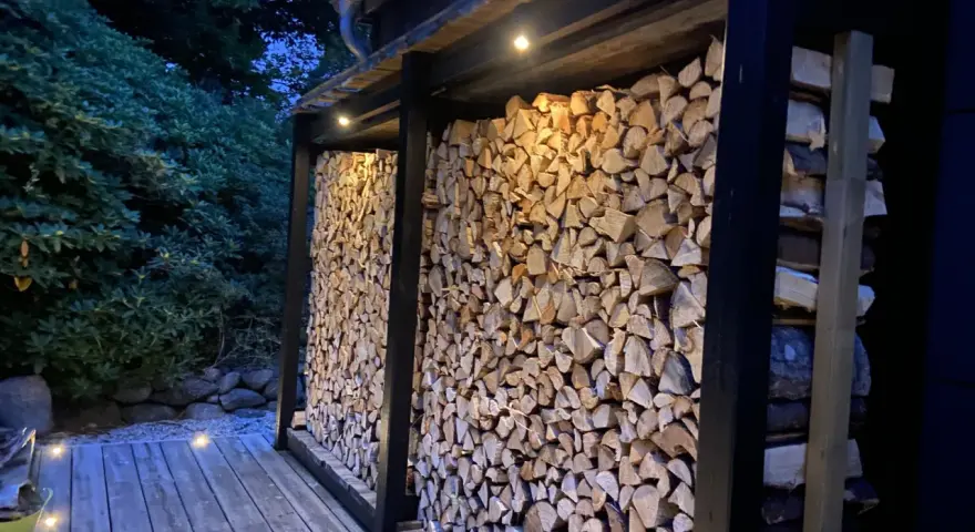 En vedbod är färdig att bygga, fylld med ved och belyst av små lampor.
