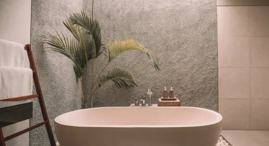 Ett modernt badrum med ett fristående badkar. En stege med vita handdukar står bredvid. En palm växer bakom badkaret. Kanske dags att måla badkar för en ny look?
