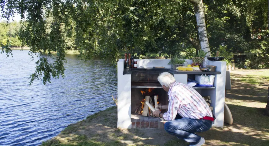 Man tänder en brasa i en nybyggd grill av tegelstenar vid en sjö.