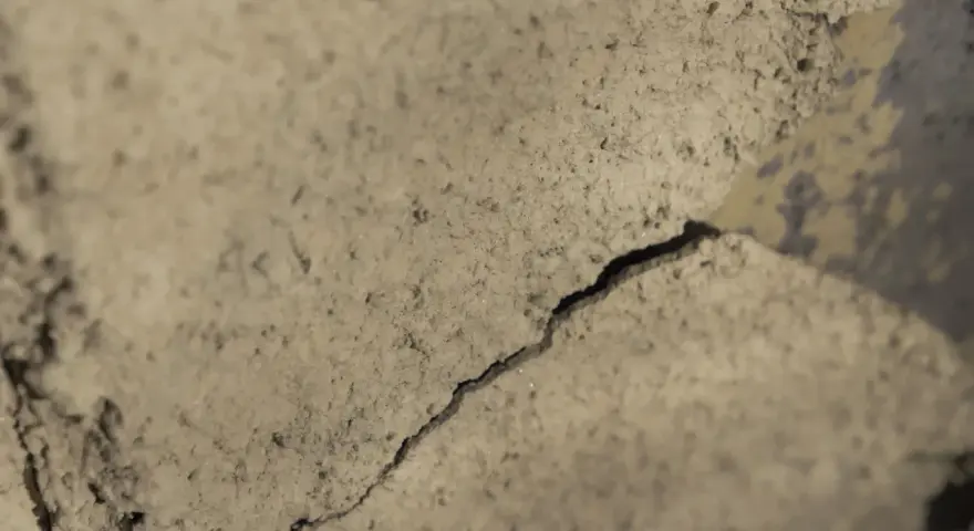 Detaljerad vy av sprucket putsbruk utomhus. Ytan är grov och ojämn med skuggor som framhäver sprickan.