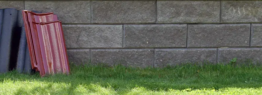 Två staplar takpannor, en svart och en röd, lutar mot en mur av grå betongblock. Undrar vad kostar takpannor?