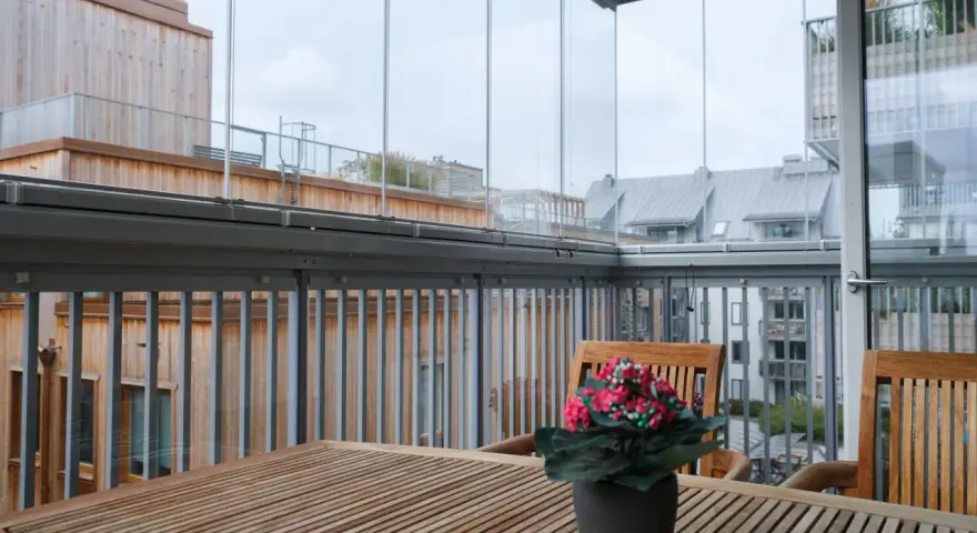Träbord och stolar på en inglasad balkong med utsikt över stadens tak. Tänk på inglasad balkong pris för din egen dröm.