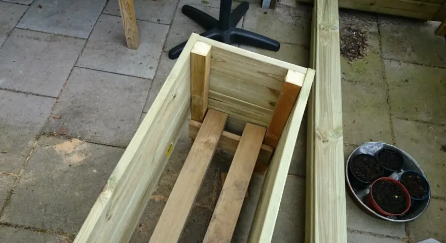 Påbörjat projekt att bygga blomlåda av tryckimpregnerat virke. Några krukor med jord står redo.