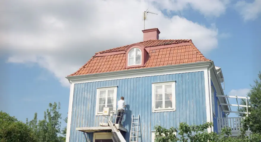 Man målar om en blå träfasad från en lift. En dropplist fasad skyddar mot regn.