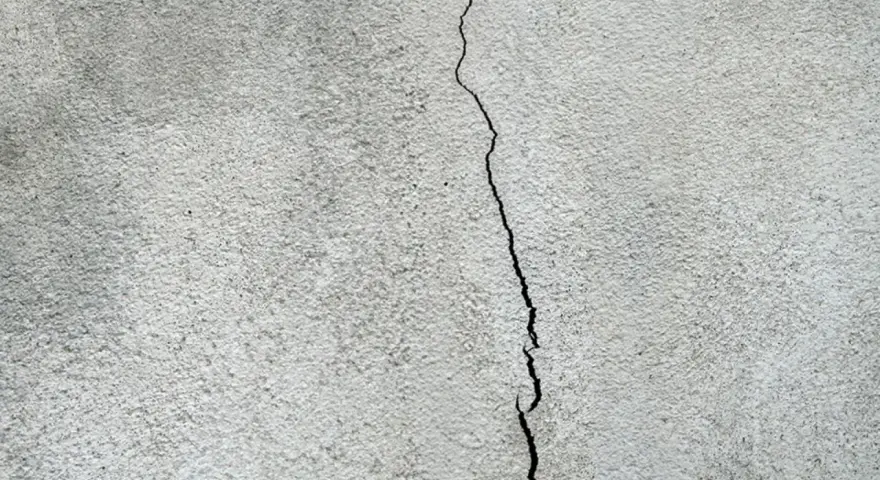 En spricka löper genom en grov, grå putsad fasad. Dags att putsa fasaden för att laga skadan.