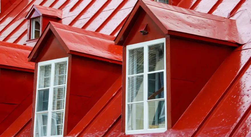Två röda takkupor med vita fönster mot ett tak av olika typer av plåttak.