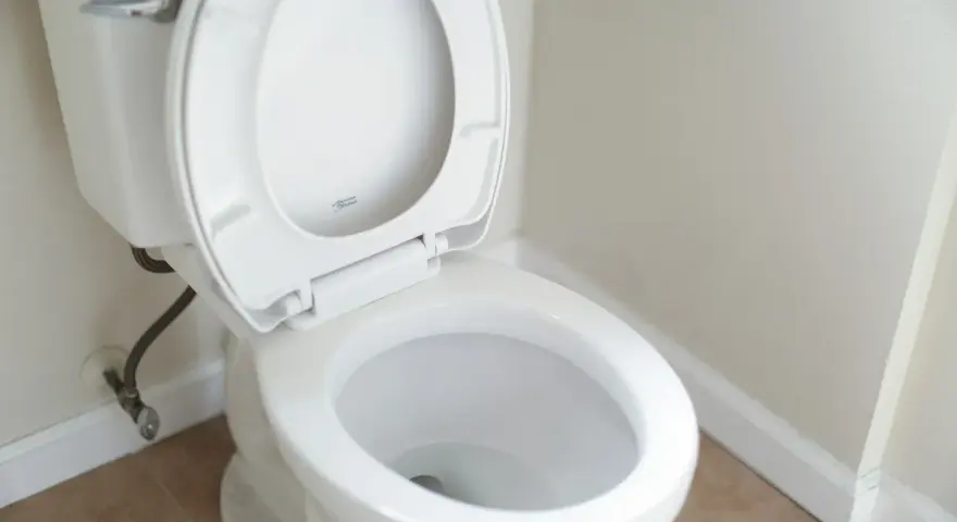 En vit toalett med öppet lock. Vattenanslutningen syns vid sidan, vilket kan tyda på ett potentiellt stopp i toaletten.