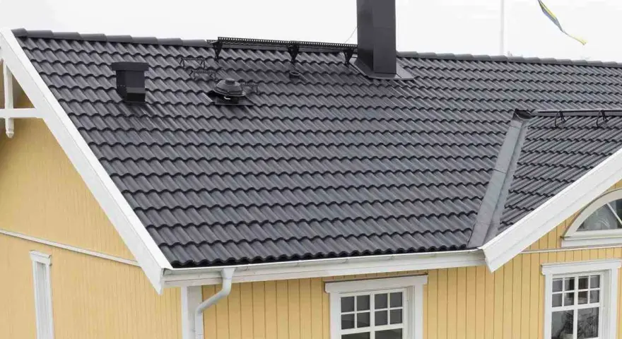 Taket har mörka takpannor, en svart skorsten och en svensk flagga. Vindskiveplåt montering syns längs takkanten.