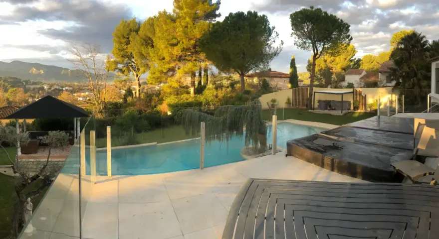 Solnedgång över en pool med trall runt om. Vackert landskap med träd och berg i bakgrunden.