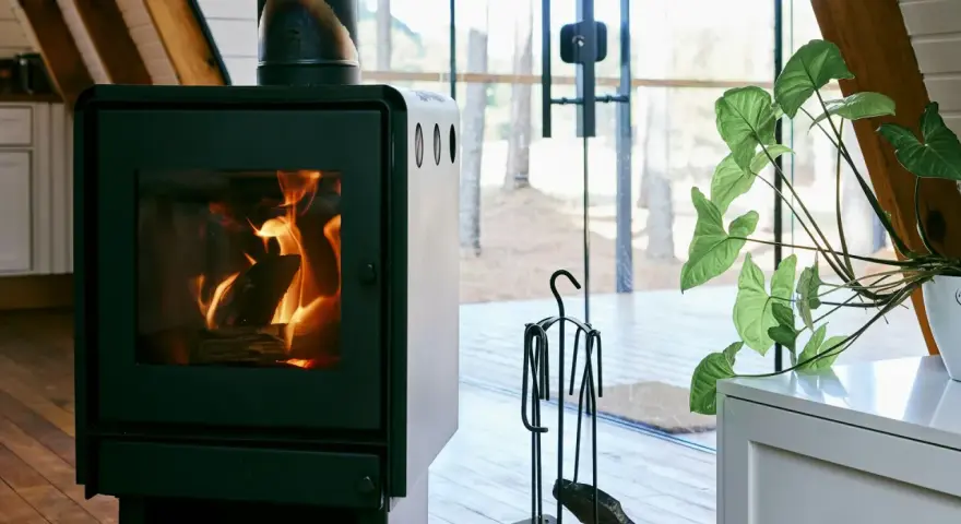 En modern kamin med sprakande eld. Bredvid står en växt och en uppsättning verktyg, allt enligt eldstadsplan regler för säkerhet.