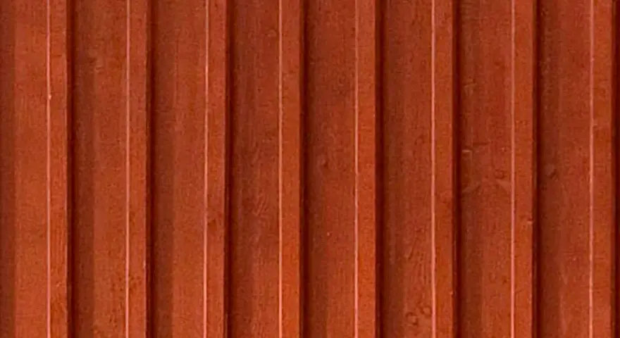 Detaljbild av en rödbrun, gammaldags lockpanel i trä. Panelen har vertikala spår och ger en känsla av traditionellt svenskt byggnadssätt.