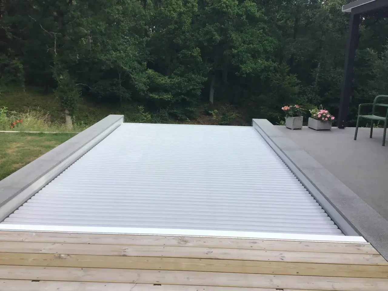 Ett modernt pooltak i vitt, perfekt för att bygga eget pooltak. Omgivet av grönskande träd och en träaltan.