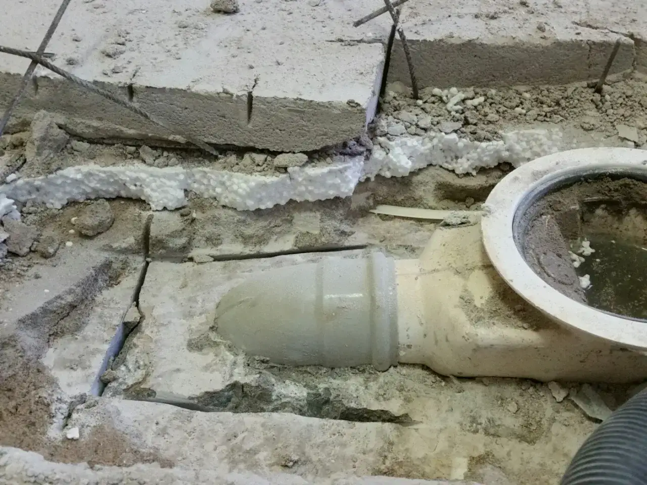 Renovering av avloppssystem hus. Synligt rör och golvbrunn i betonggolv under arbete.