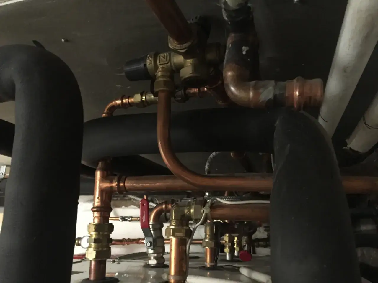 Detaljerad vy av rördragning för att installera varmvattenberedare. Kopparrör och isolerade rör syns tydligt.