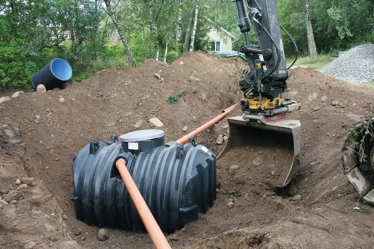 Grävmaskin installerar enskilt avlopp. En stor plasttank placeras i marken, vilket kan påverka enskilt avlopp kostnad.