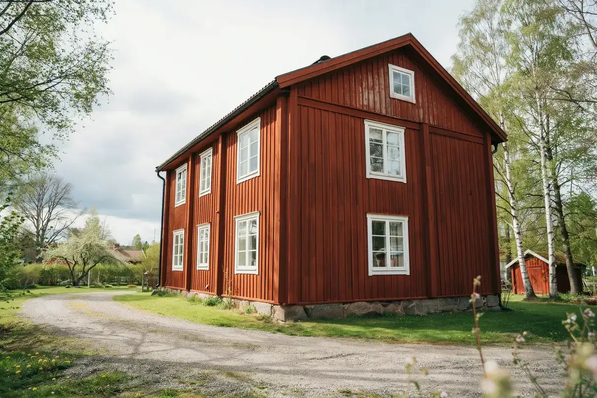 Rött trähus med vita fönster, redo att måla huset för sommaren. Grusväg leder fram till huset.