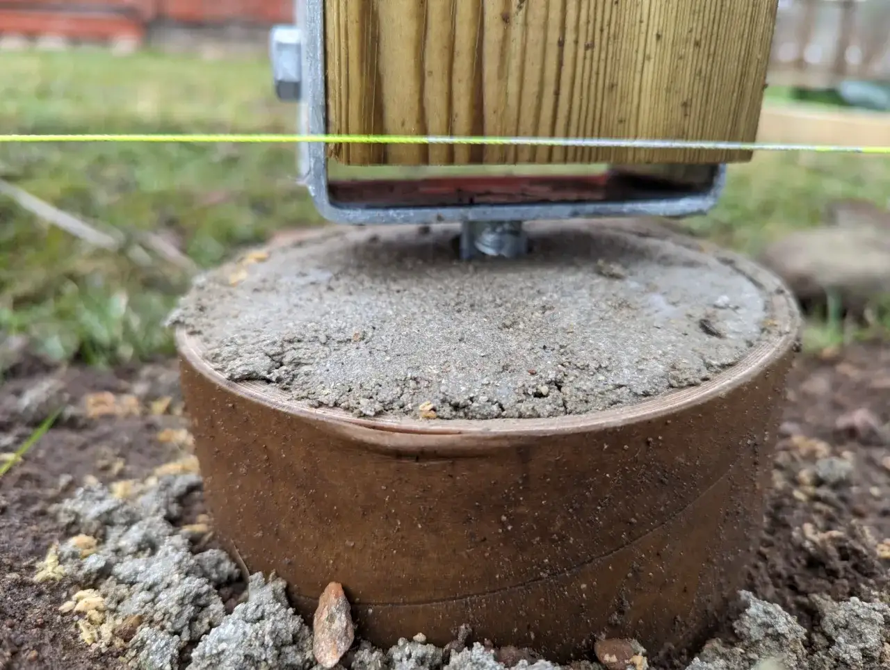 En nybyggd stolpe för ett staket vilar på en gjuten plint. En snörning visar höjden.