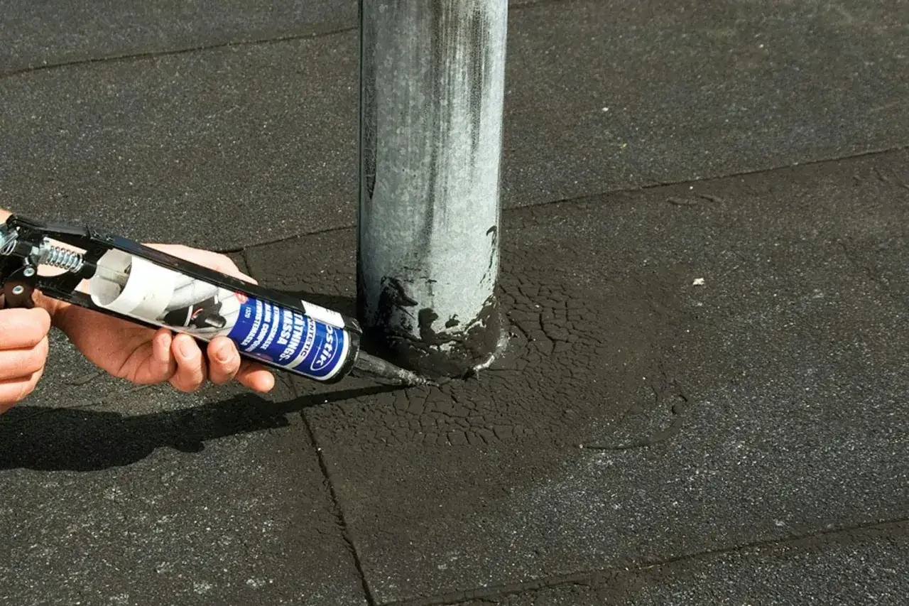 En hand använder en fogpistol för att laga papptak runt ett rör.