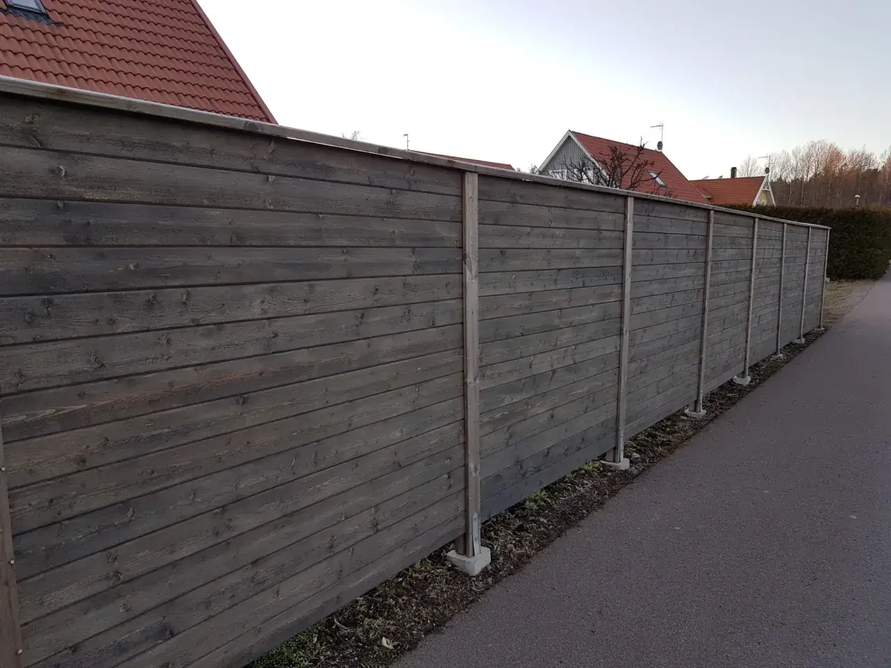 En lång, mörk trästaket med liggande panel. Staketet är byggt för att ge insynsskydd och avgränsa en tomt.