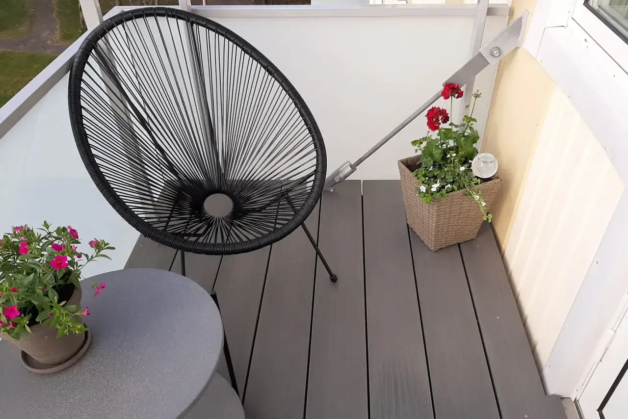 En svart stol och ett runt bord står på ett trallgolv på balkongen. Blommor i krukor ger färg åt scenen.
