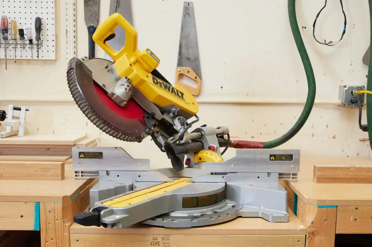 En gul DeWalt kap- och geringssåg står redo för arbete. Bredvid hänger två gamla handsågar, en samling av olika sågar för alla projekt.