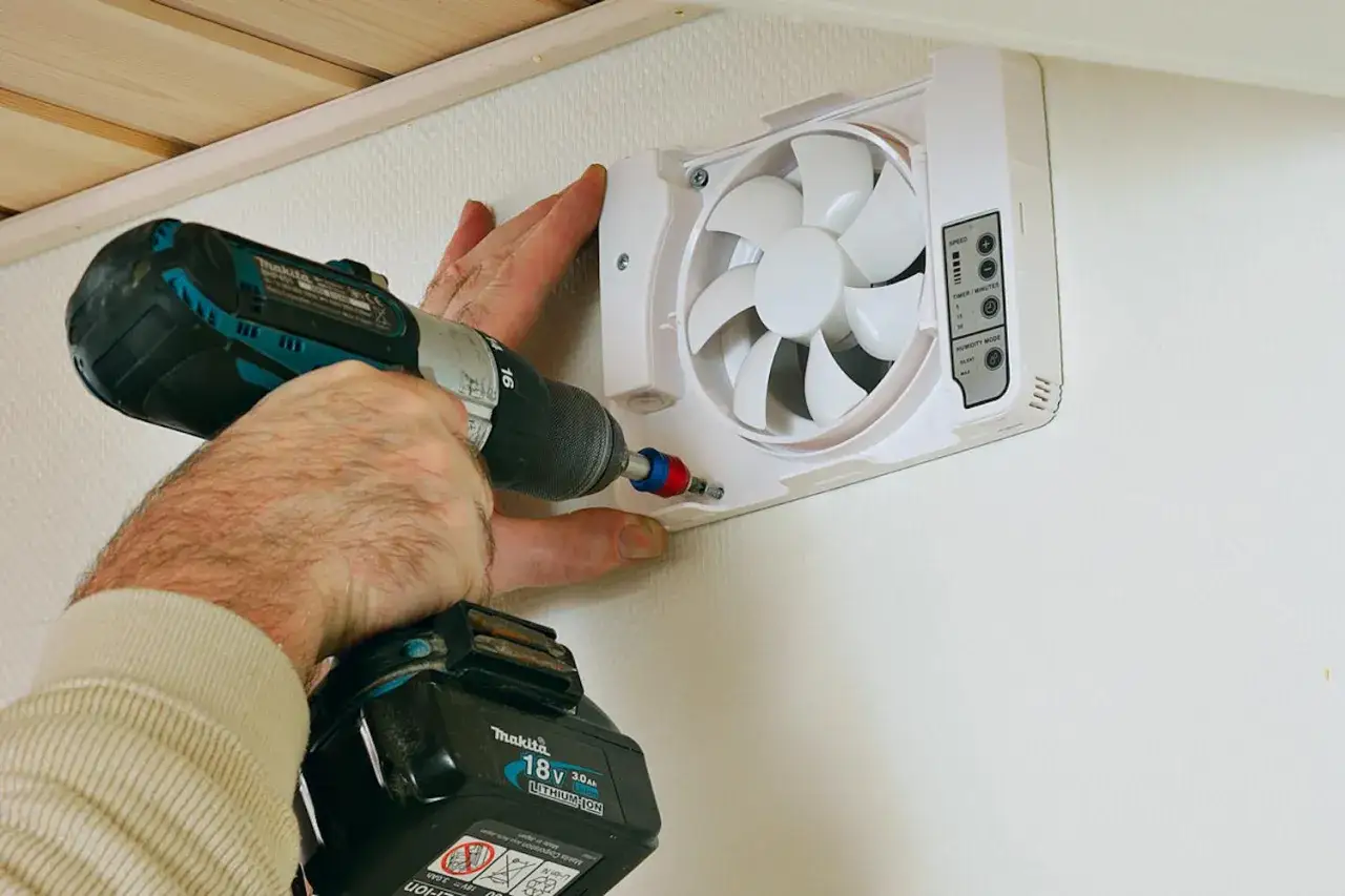 Montering av en ny fläkt för ventilation i badrummet. En borrskruvdragare används för att fästa enheten.