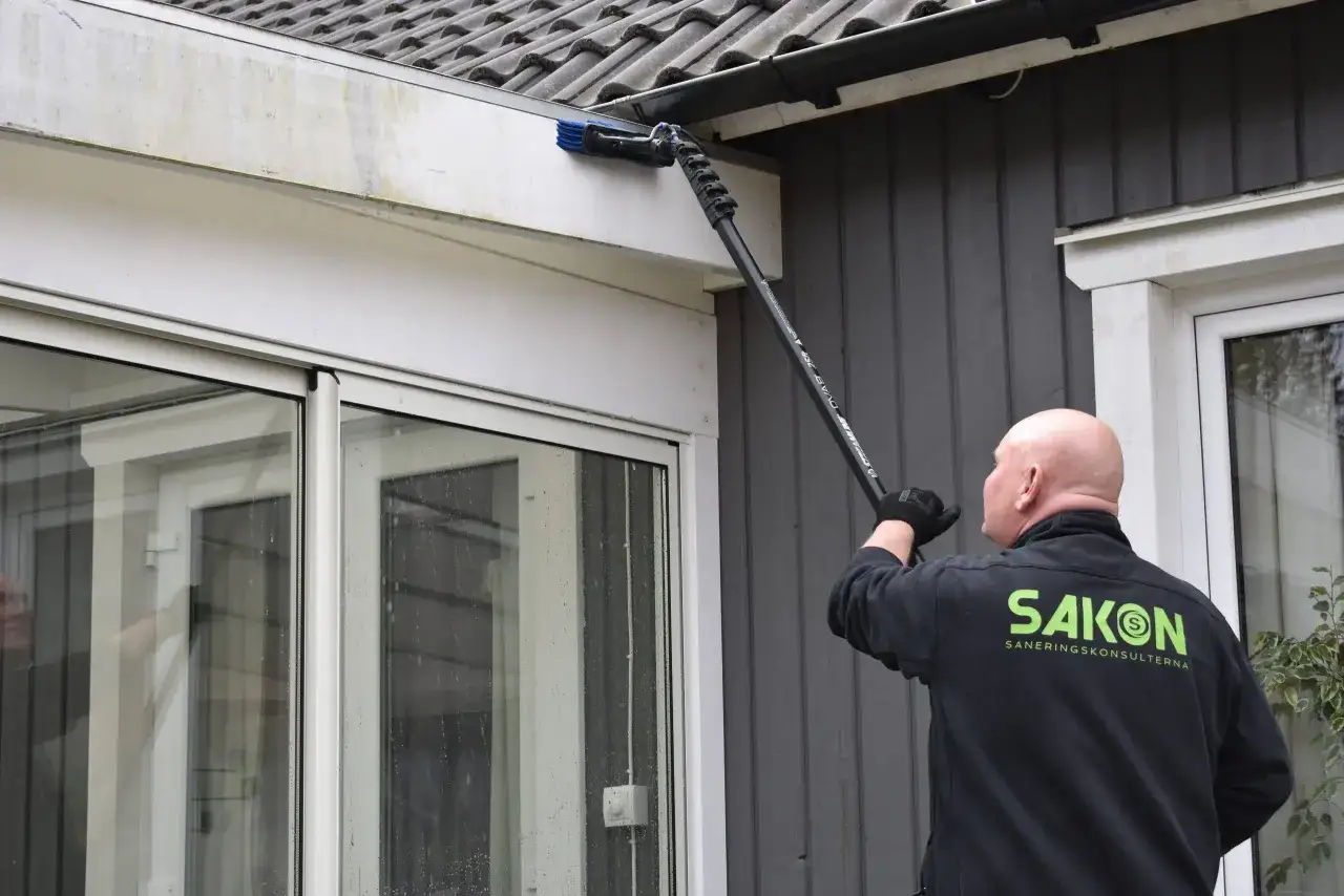 Man rengör takrännan från alger på fasaden med en lång borste.