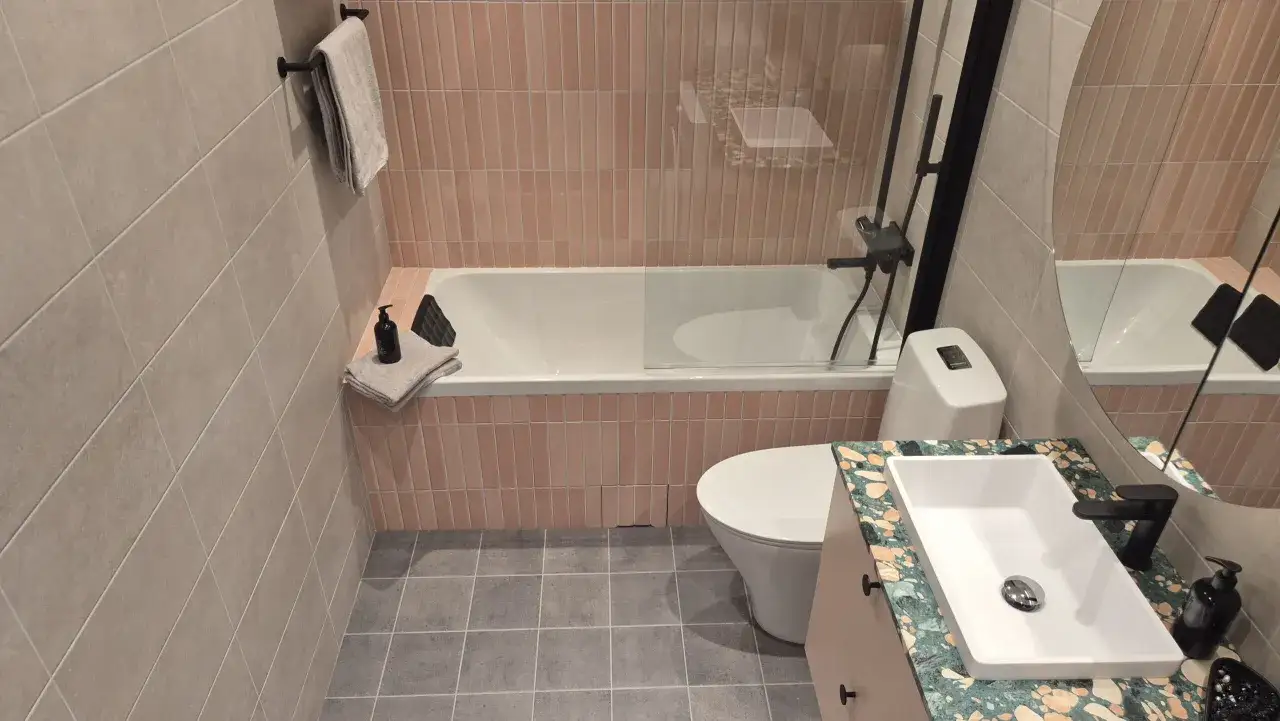Modernt badrum med rosa kakel vid badkaret, en vit toalett och ett handfat med en unik bänkskiva. Perfekt för en renovering av badrum.