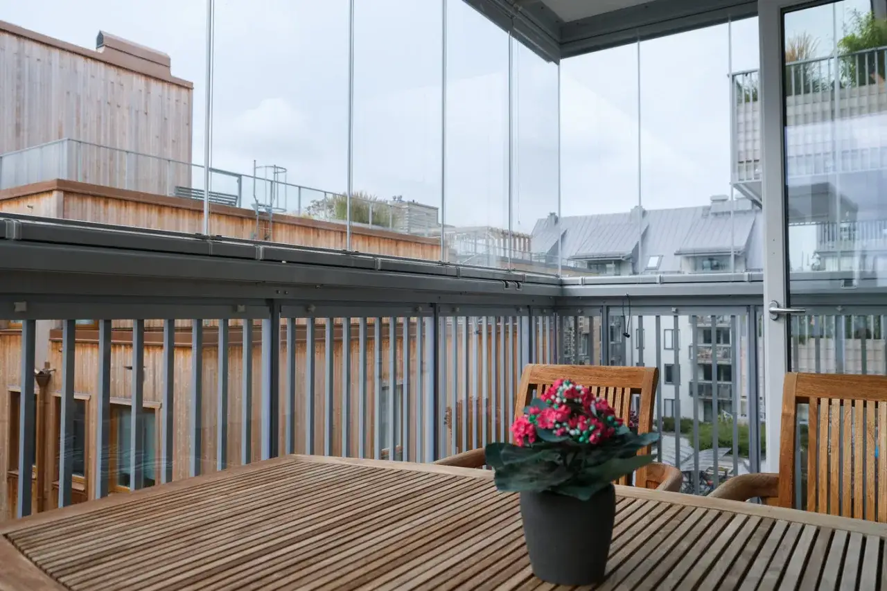 Träbord och stolar på en inglasad balkong med utsikt över stadens tak. Tänk på inglasad balkong pris för att maximera din uteplats.
