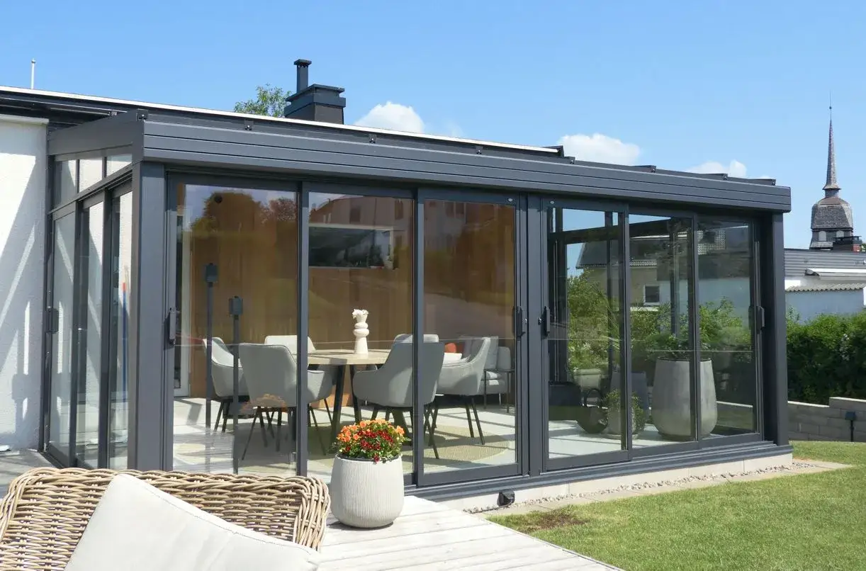 Modernt uterum med stora glaspartier, perfekt för att bygga poolhus. Möblerad matplats inomhus.