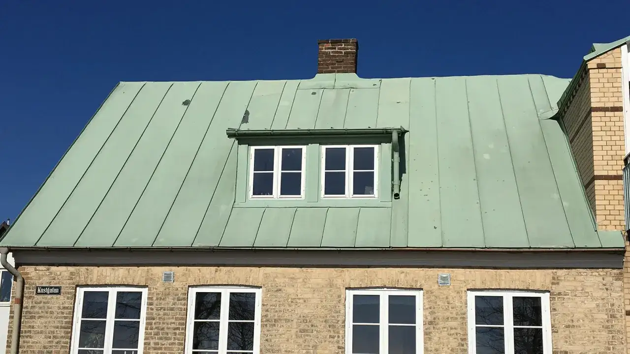 Ett hus med ett grönt plåttak gammal stil, tegelvägg och vita fönster under en klarblå himmel.