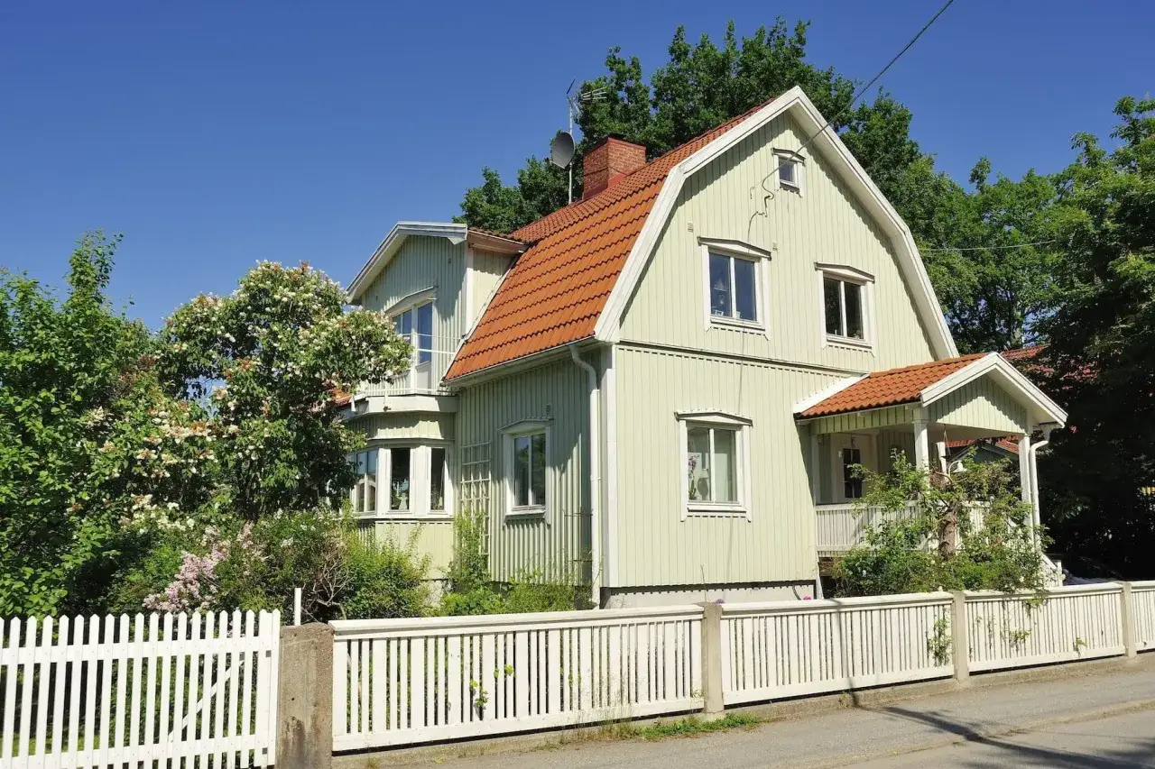 Ett ljust grönt trähus med tegeltak, omgivet av grönska. Kanske dags att byta fasad för att fräscha upp huset?