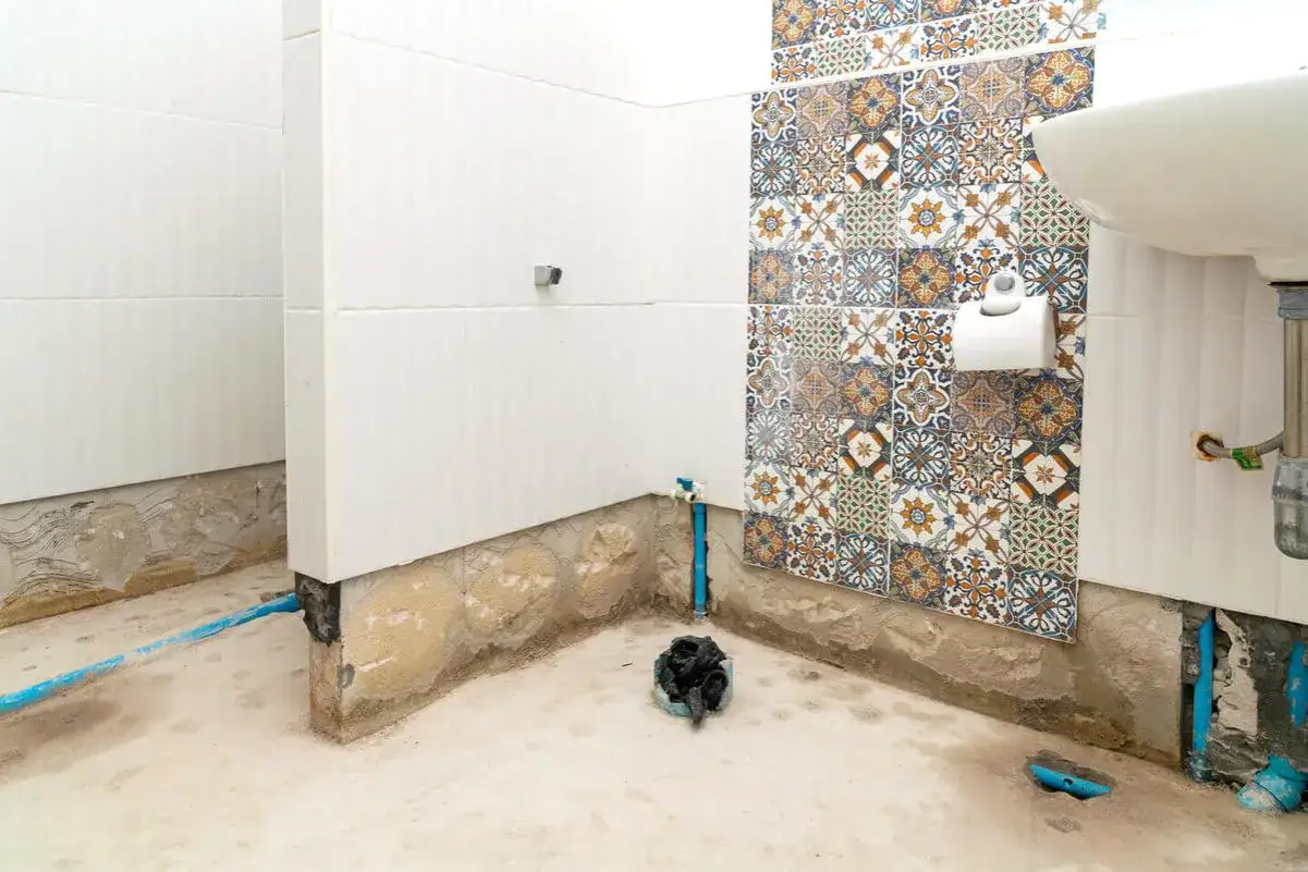Renovering av badrum med synliga rör och en bit av en vacker kakelvägg. Förberedelser för att laga våtrumsmatta.