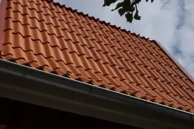Rött tegeltak med rännsten. Taket har en minimal taklutning för betongpannor, vilket ger ett stilrent utseende.