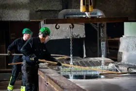 Två arbetare i skyddsutrustning hanterar metall som doppas i ett bad. Processen för varmförzinkning pris kan variera beroende på material och storlek.