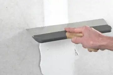 Handen spacklar en vägg med en bred spackel. Arbetet med att kapa gipsskiva kan nu fortsätta.