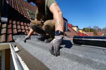 Takläggare arbetar med att byta takpapp. En ny rulle takpapp ligger redo. Undrar du över byta takpapp kostnad?