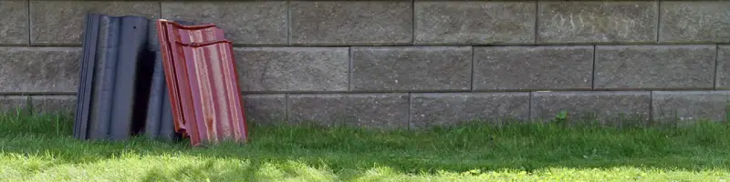 Två staplar takpannor, en svart och en röd, lutar mot en mur av grå betongblock. Undrar vad kostar takpannor?