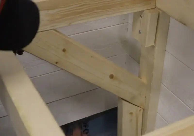 En person håller på att såga snett en träbit som ska bli en del av en konstruktion.